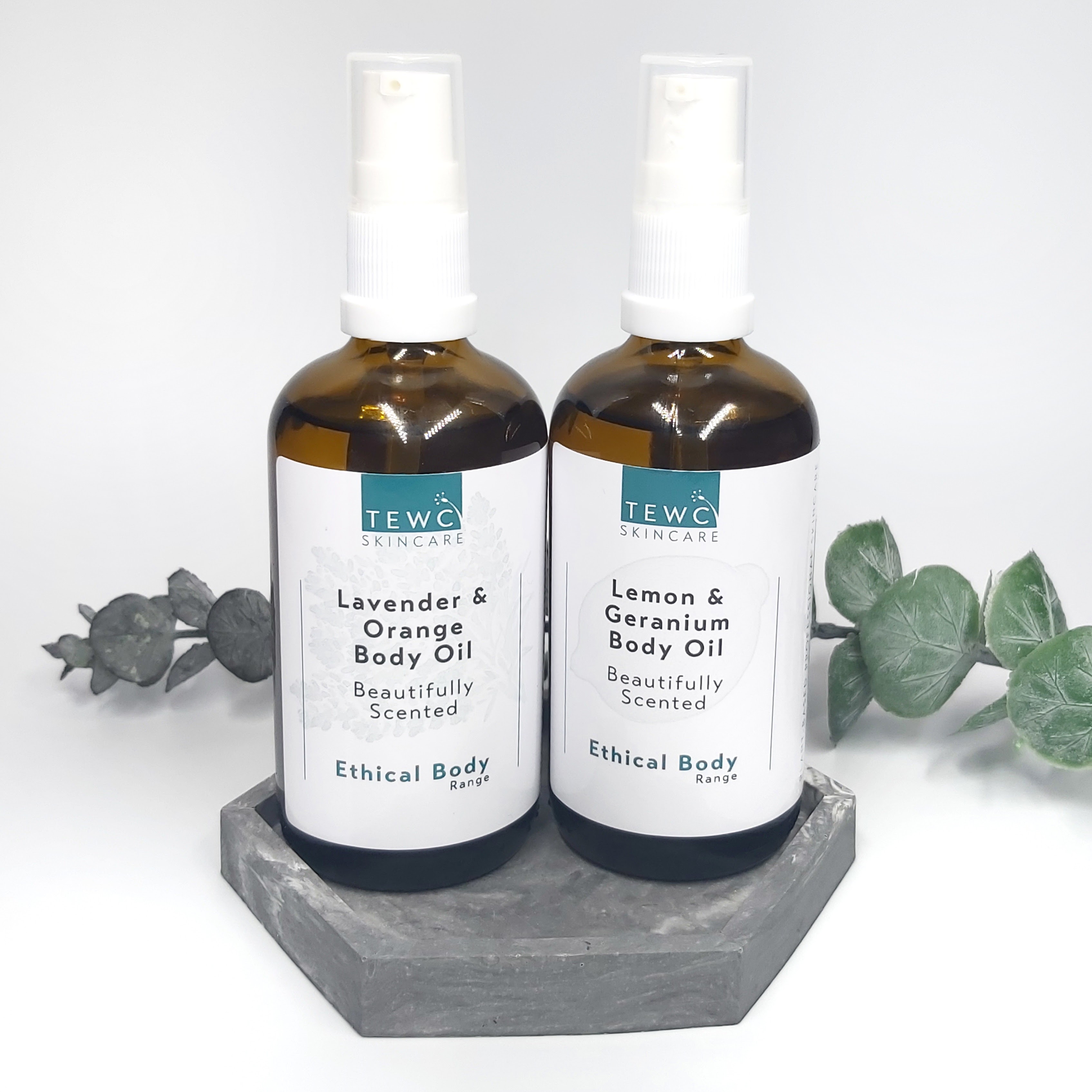 Two TEWC Skincare Body Oils in a grey, clay dish with a sprig of eucalyptus in the background. Review by Beauty Folio