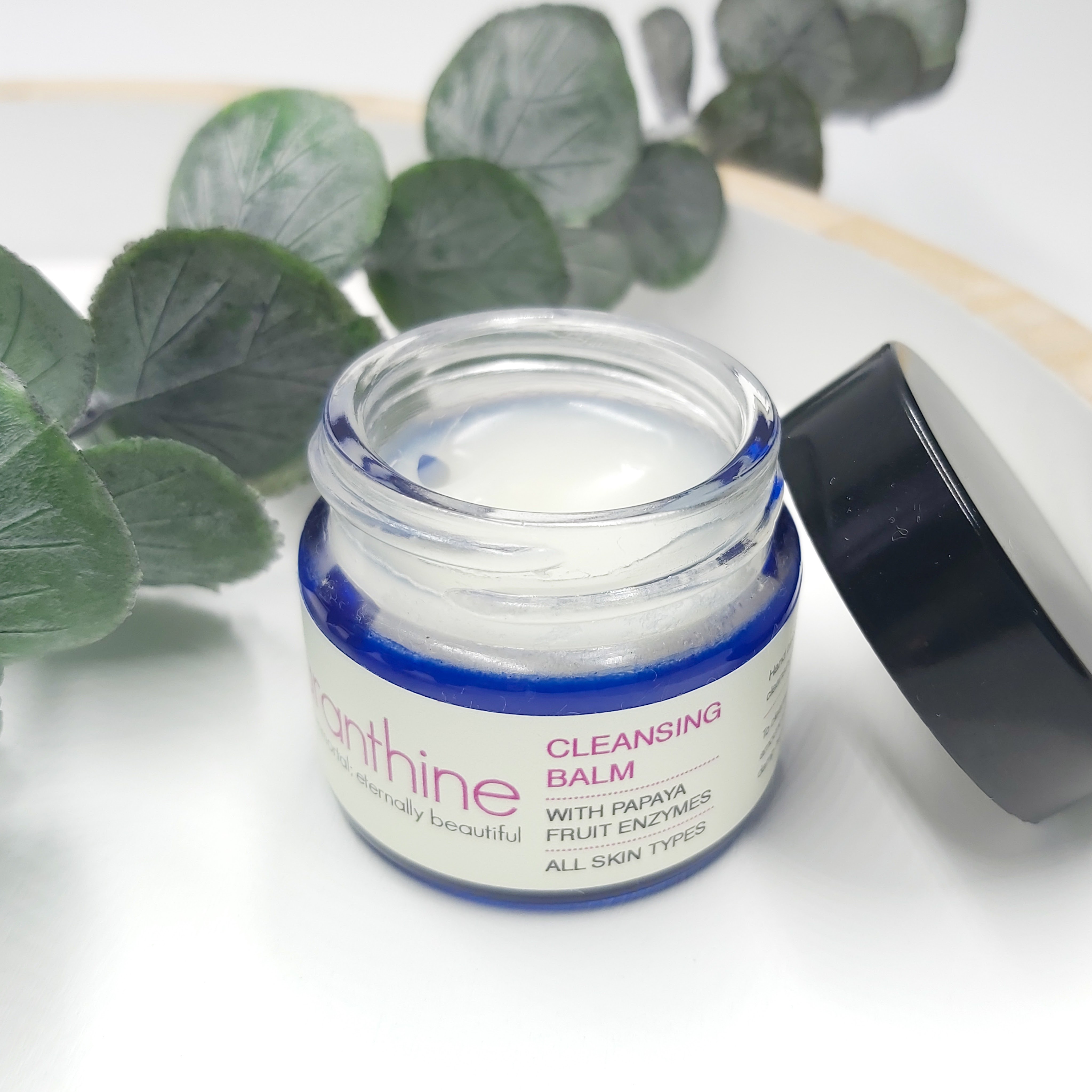 Amaranthine Cleansing Balm open on a tray with a spring of eucalyptus foliage. 