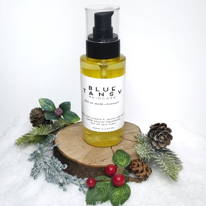 Blue Tansy Skincare Cleansing Oil bottle sits on a log slice with snow and Christmas foliage. Natural Beauty Christmas Gift Guide by Beauty Folio.