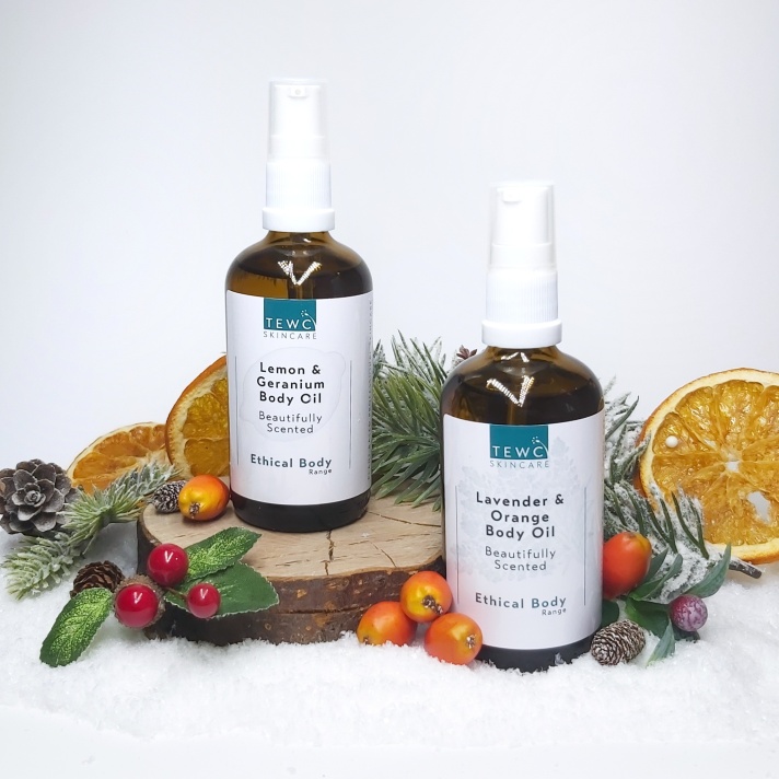 Two TEWC Body Oil bottles standing on a log slice with Christmas foliage and orange slices. Natural Beauty Christmas Gift Guide by Beauty Folio